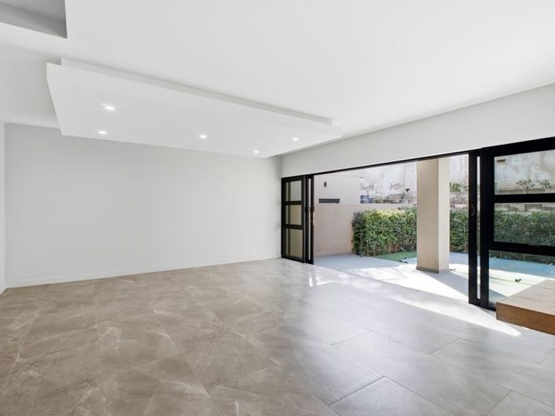 Spacious, modern living area featuring large format floor tiles, recessed ceiling lighting, and seamless access to a covered patio through wide sliding glass doors.