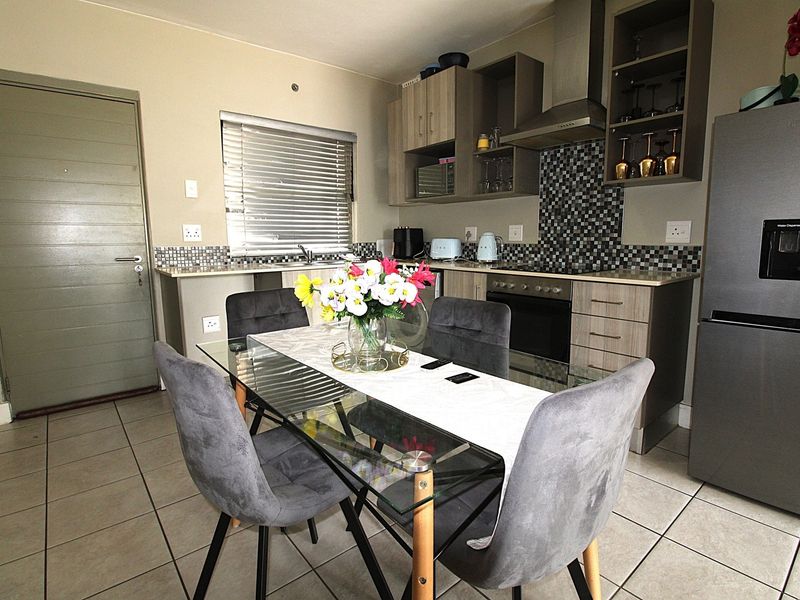 Open-plan kitchen and dining area featuring modern cabinetry, mosaic tile backsplash, built-in oven and hob, and neutral tiled flooring.