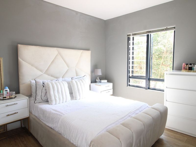 A well-maintained bedroom featuring neutral grey walls, laminate flooring, and a large window with fitted blinds providing natural light.