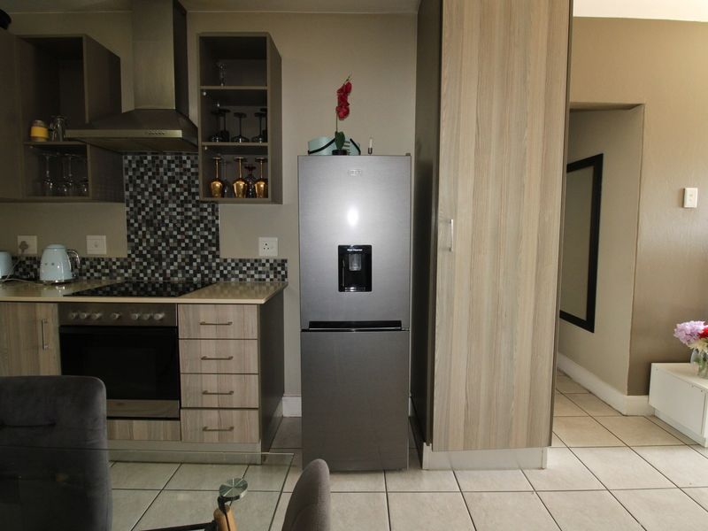 A functional kitchen featuring modern wood-finish cabinetry, a mosaic tile backsplash, integrated oven and hob, and neutral tiled flooring.