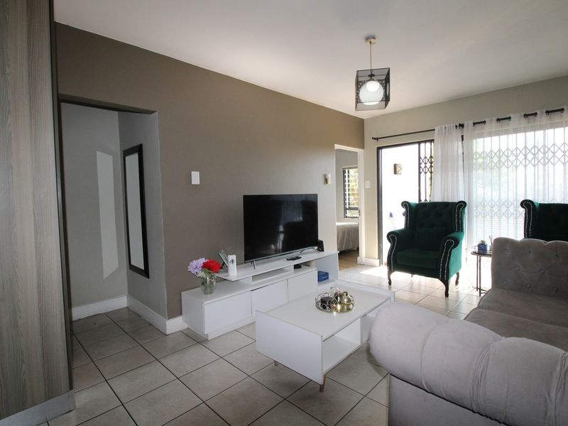 A living room featuring tiled flooring, a pendant light, and a sliding glass door with a security gate leading to an outdoor area.