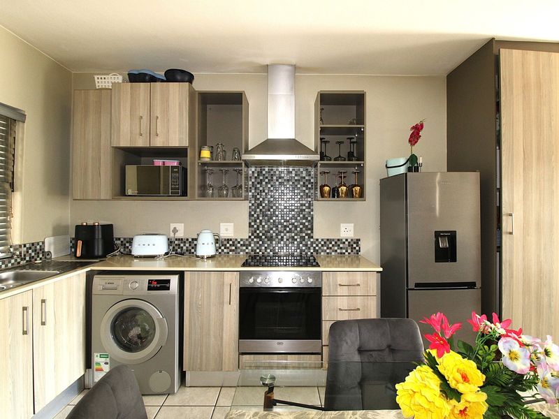 Modern kitchen featuring wood-look cabinetry, mosaic tile backsplash, integrated stainless steel appliances, and a functional layout with ample storage and counter space.