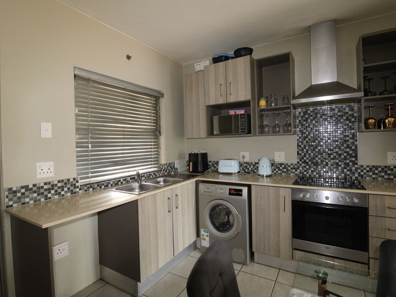 A functional kitchen featuring modern wood-look cabinetry, mosaic tile backsplash, integrated oven and hob, and a stainless steel sink with tiled flooring.