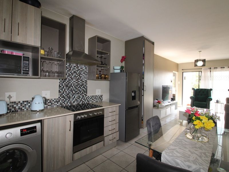 Open-plan kitchen and living area featuring modern cabinetry, integrated appliances, mosaic tile backsplash, and tiled flooring leading to a bright patio space.