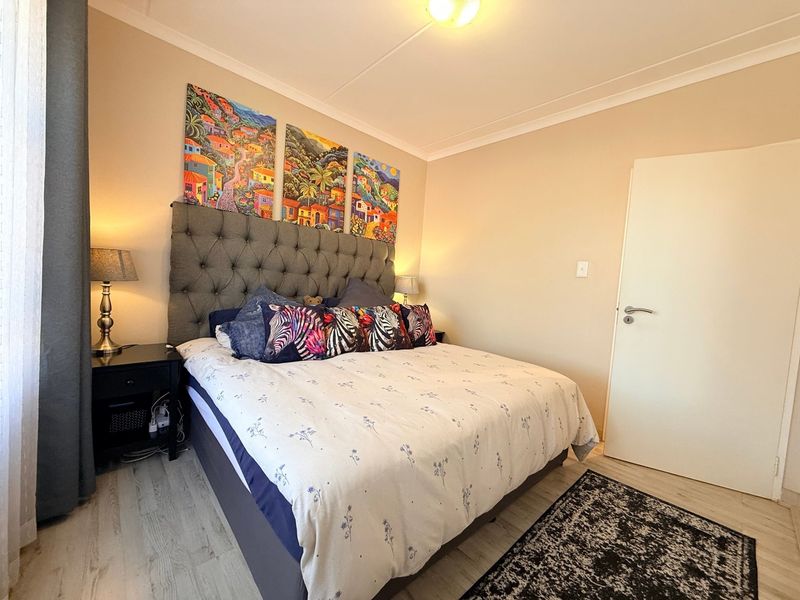 A well-maintained bedroom featuring light-toned laminate flooring, neutral wall finishes, and classic cove cornicing.