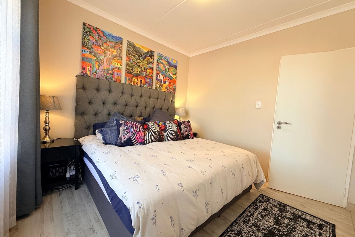 A well-maintained bedroom featuring light-toned laminate flooring, neutral wall finishes, and classic cove cornicing.