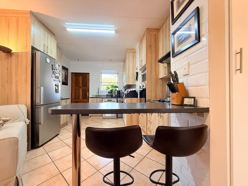 A functional kitchen featuring light wood cabinetry, subway tile backsplash, ceramic tiled flooring, and a convenient breakfast bar for casual dining.