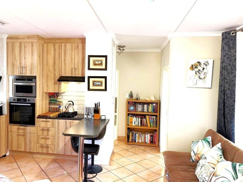 Open-plan living area featuring a compact kitchen with built-in appliances, breakfast bar, and tiled flooring throughout.