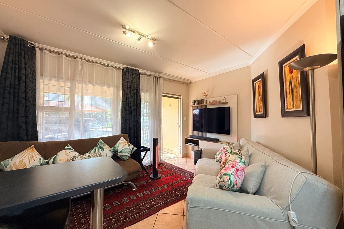 A comfortable living room featuring tiled flooring, track lighting, and a built-in media console, with direct access to an outdoor area via a sliding door.