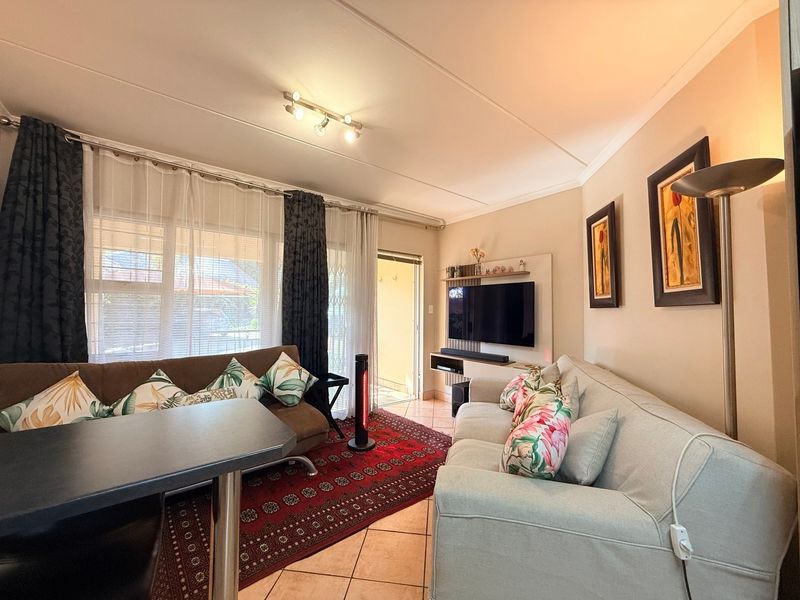 A comfortable living room featuring tiled flooring, track lighting, and a built-in media console, with direct access to an outdoor area via a sliding door.