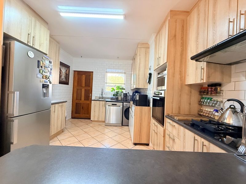 A functional kitchen featuring light wood-finish cabinetry, subway tile backsplash, integrated appliances, and tiled flooring, offering a clean and practical workspace.