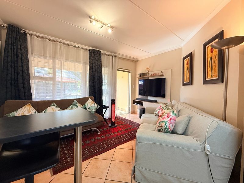 A comfortable living room featuring ceramic tile flooring, track lighting, and a built-in media console with direct access to an outdoor patio area.