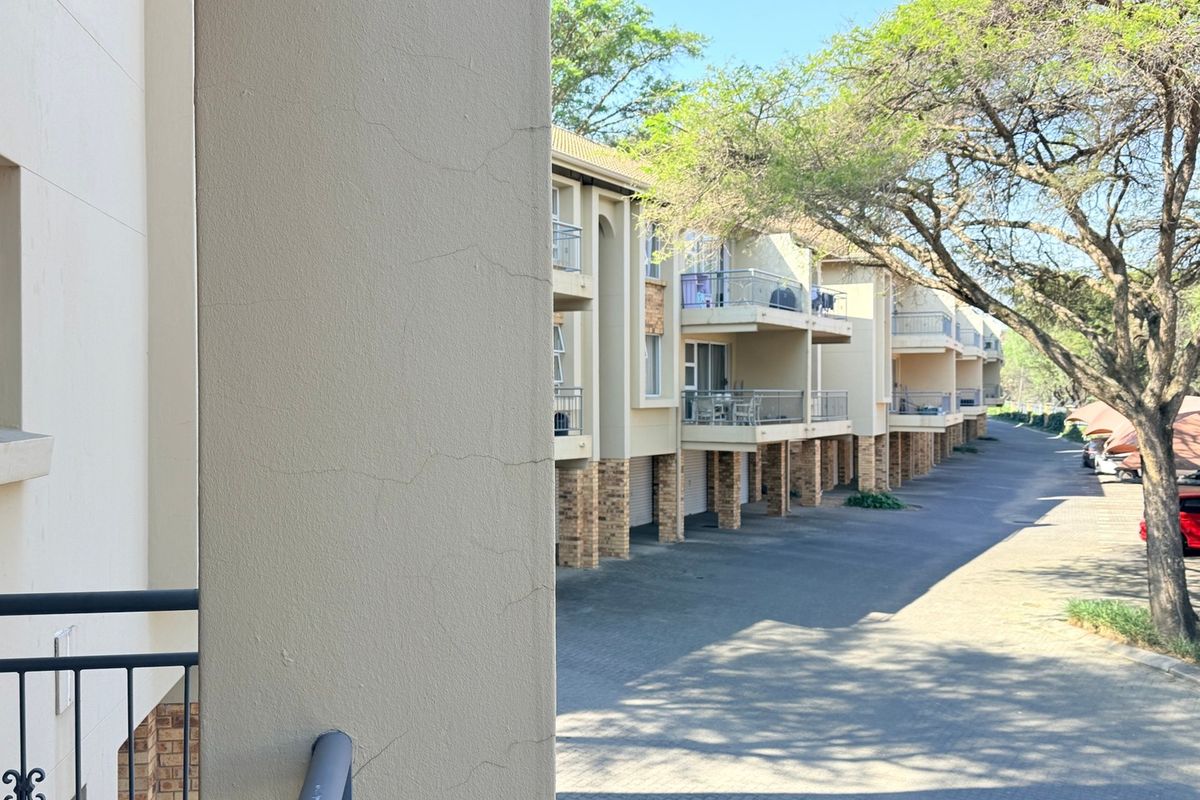 Exterior view of an apartment complex featuring multiple balconies, brick support pillars, and a paved driveway area.