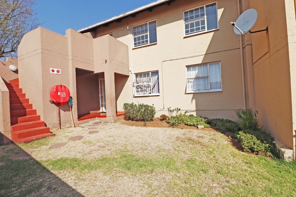 Rear view of an apartment building featuring a small garden area, concrete staircase, and exterior fire safety equipment.