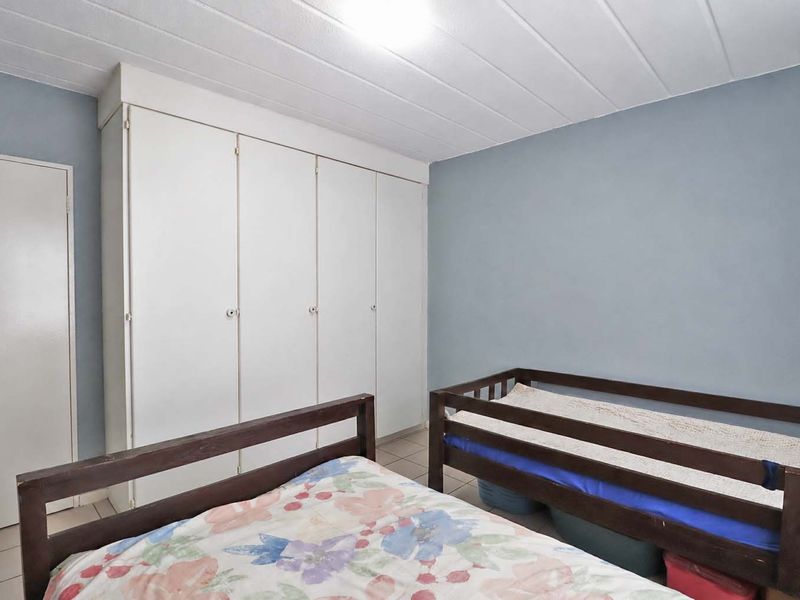 A functional bedroom featuring built-in cupboards, tiled flooring, and a panelled ceiling, offering a neutral base for personalization.
