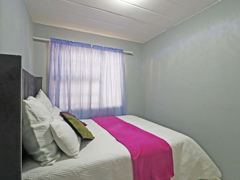 A compact bedroom featuring neutral wall finishes and a window with a fitted curtain rod.