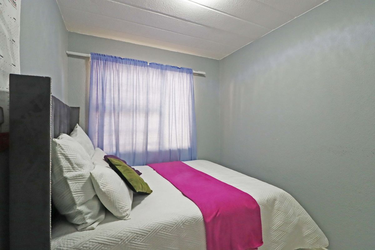 A compact bedroom featuring neutral wall finishes and a window with a fitted curtain rod.