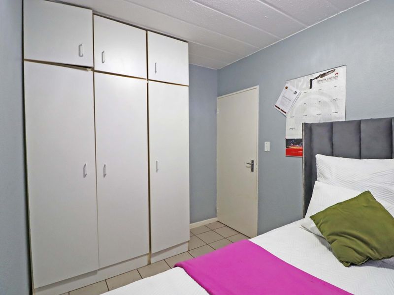 A bedroom featuring built-in white cupboards, tiled flooring, and a neutral wall finish.