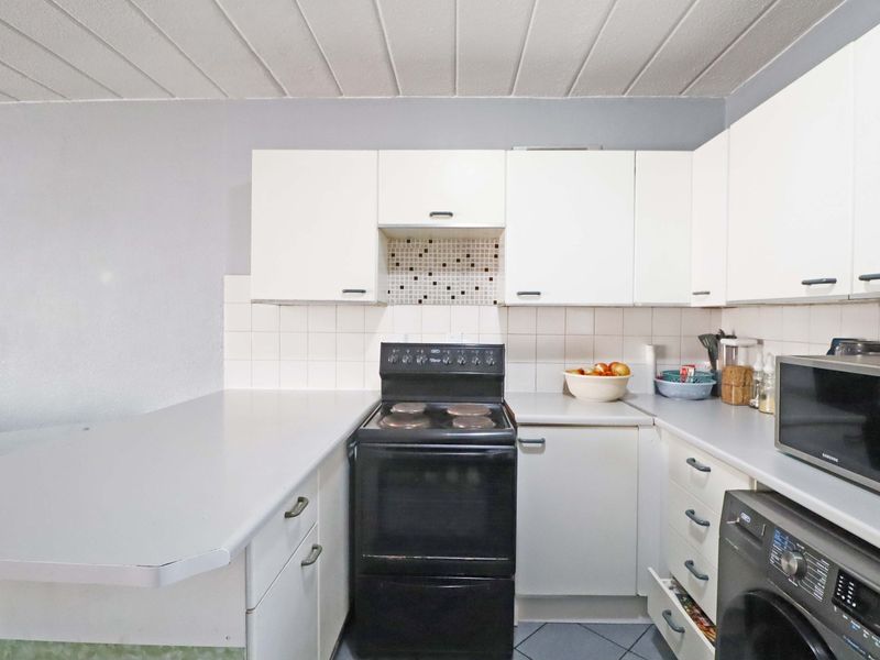 Compact kitchen featuring white cabinetry, tiled backsplash, and a freestanding stove, offering a functional layout with potential for modern updates.
