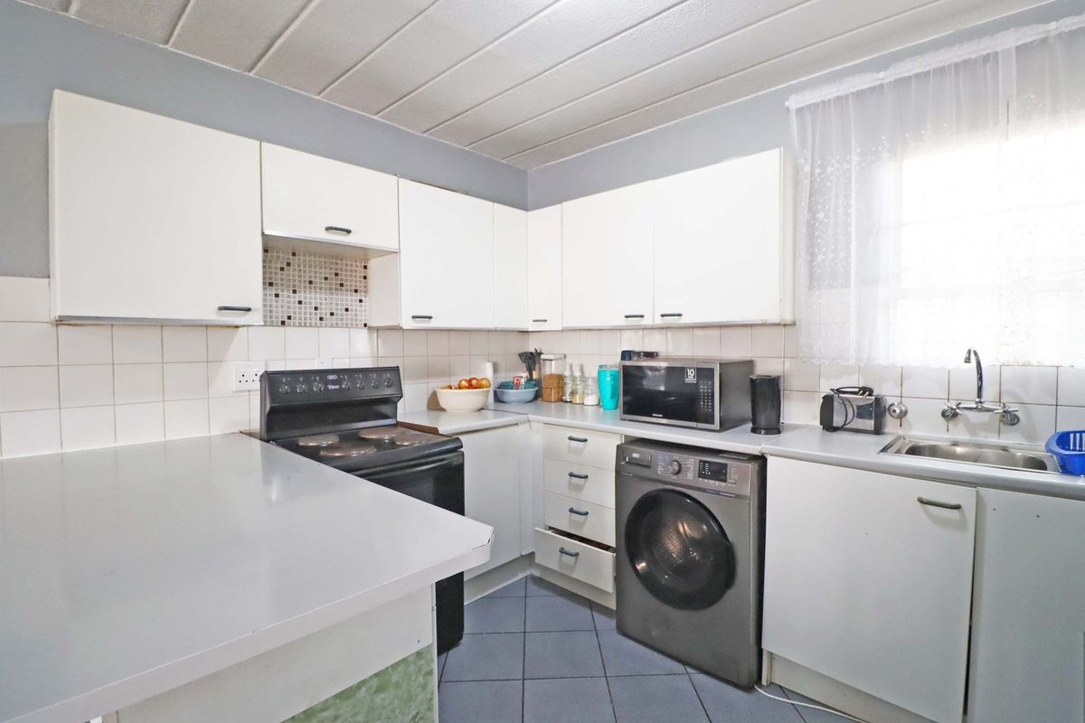 Functional kitchen featuring white built-in cabinetry, laminate countertops, tiled backsplash, and integrated electric stove with space for laundry appliances.