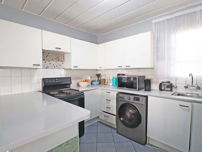Functional kitchen featuring white built-in cabinetry, laminate countertops, tiled backsplash, and integrated electric stove with space for laundry appliances.