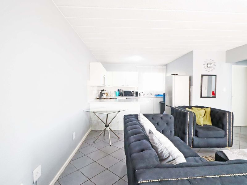 Open-plan living area featuring tiled flooring and a functional kitchen with white cabinetry and countertop space.