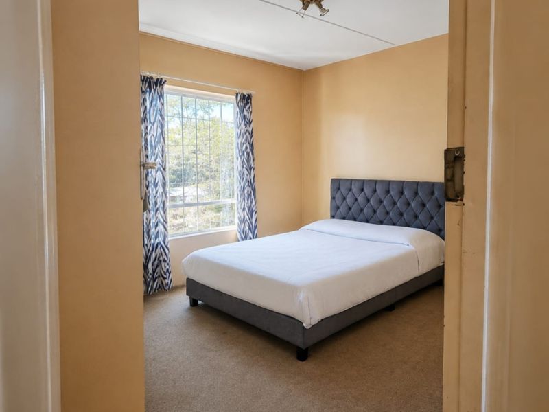 A bedroom featuring carpeted flooring, a window with security bars, and a central ceiling light fixture.