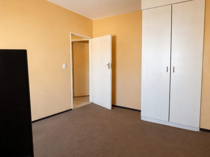 A vacant bedroom featuring neutral wall paint, carpeted flooring, and a built-in wardrobe, offering a blank canvas for personalization.