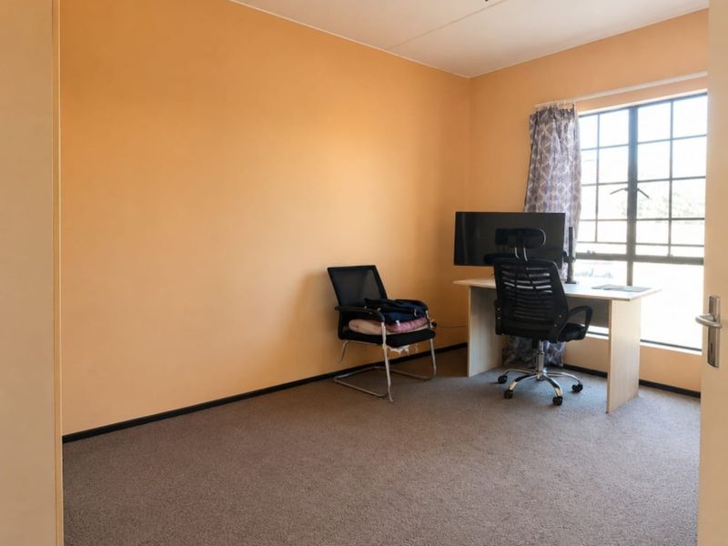 A functional bedroom featuring carpeted flooring, a large grid-pattern window, and neutral wall finishes, suitable for use as a bedroom or home office.