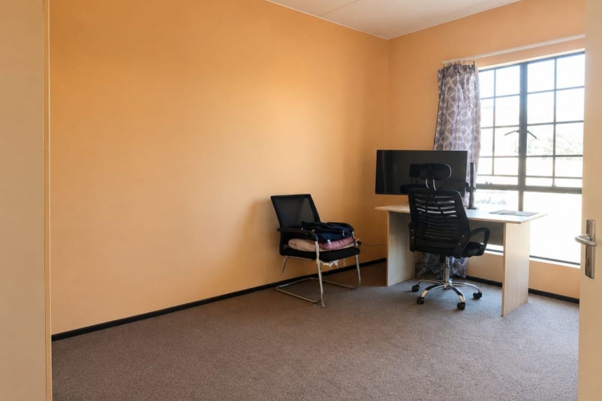 A functional bedroom featuring carpeted flooring, a large grid-pattern window, and neutral wall finishes, suitable for use as a bedroom or home office.