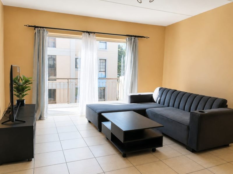 A living room featuring tiled flooring and a sliding glass door providing access to a balcony, with neutral wall tones.