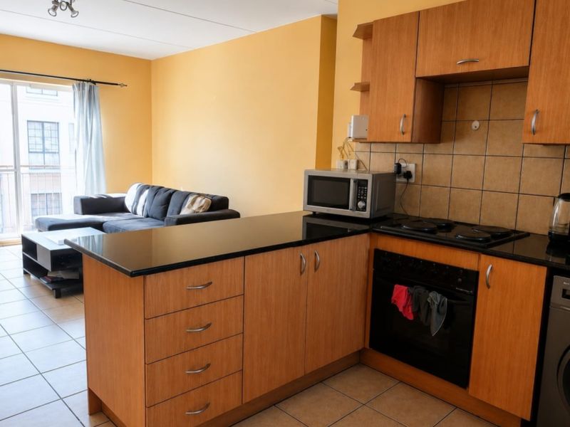 Open-plan kitchen and living area featuring wood-finish cabinetry, black granite countertops, integrated oven and hob, and direct access to a balcony.