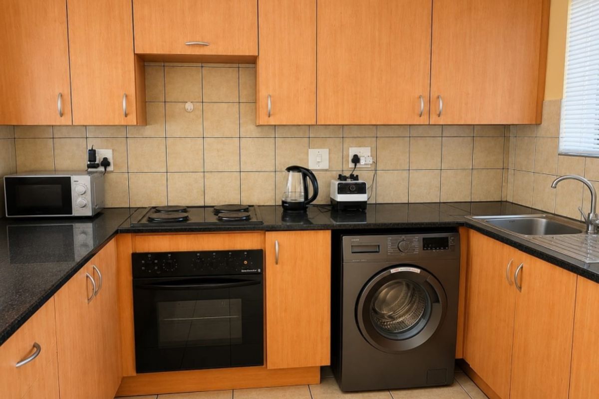 A functional kitchen featuring light wood-finish cabinetry, dark granite countertops, a built-in oven, electric hob, and integrated space for a washing machine.