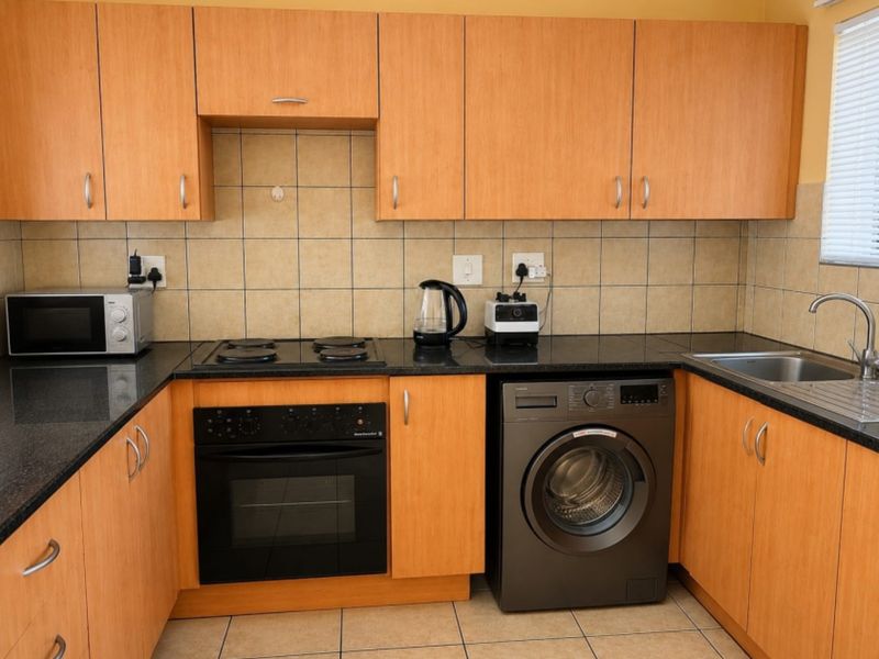 A functional kitchen featuring light wood-finish cabinetry, dark granite countertops, a built-in oven, electric hob, and integrated space for a washing machine.