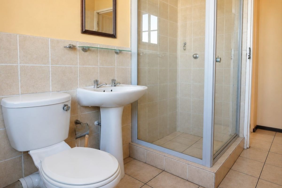 A functional bathroom featuring a pedestal basin, toilet, and a glass-enclosed shower with neutral wall and floor tiling.