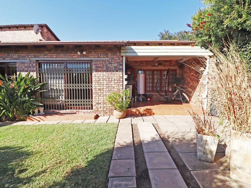 Rear exterior view of the townhouse featuring a brick facade, a covered patio area, and a small private garden with a paved walkway.
