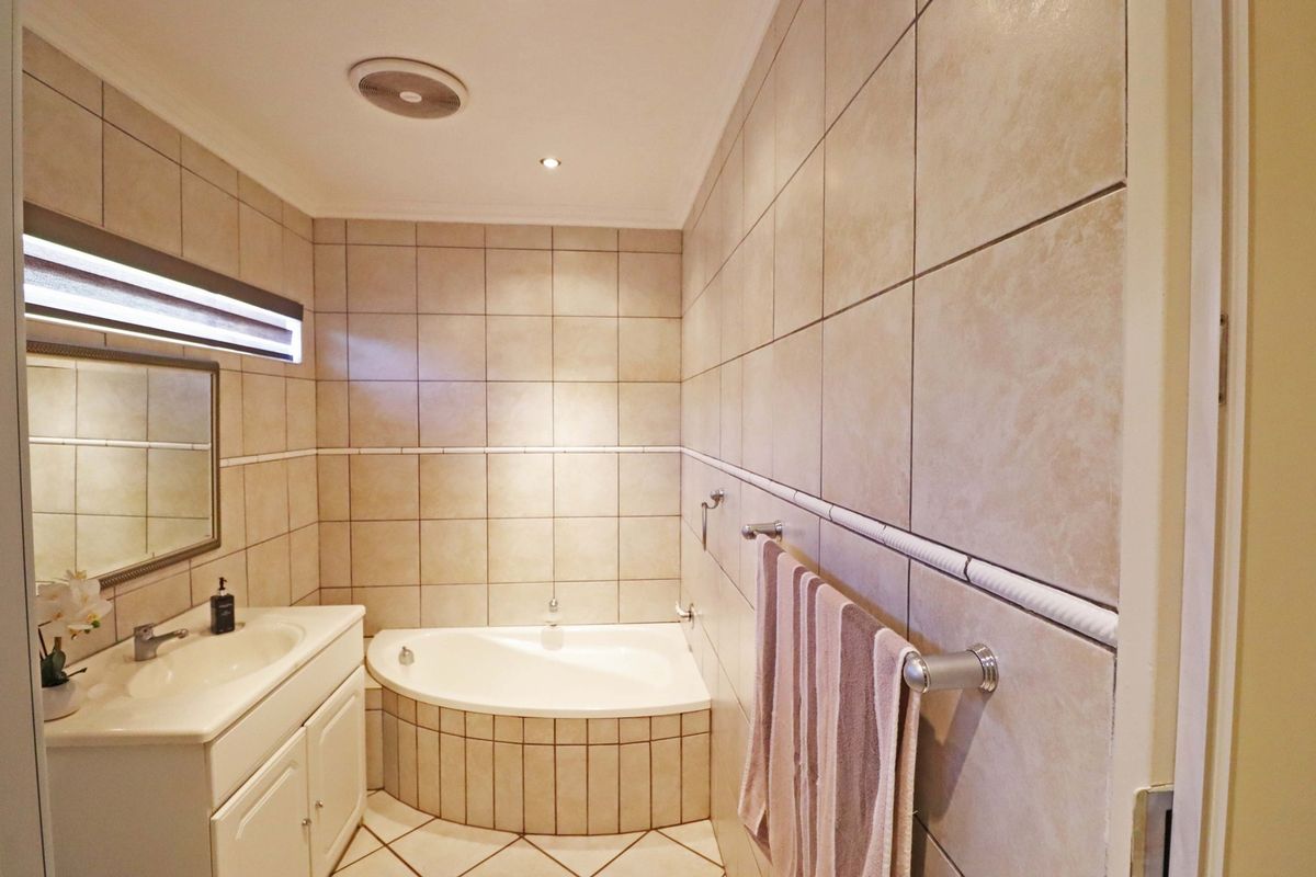 A well-maintained bathroom featuring a corner bathtub, built-in vanity with basin, and neutral floor-to-ceiling wall tiling.