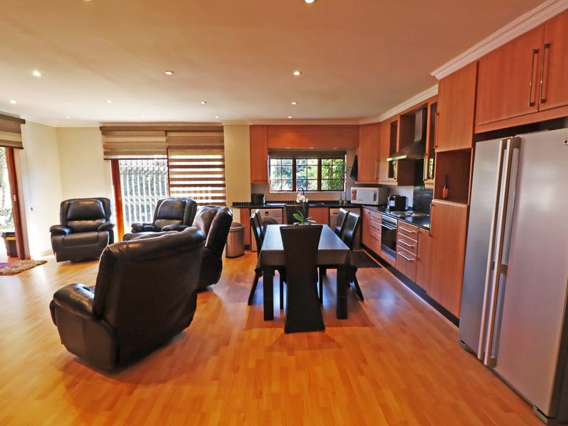 Spacious open-plan living and kitchen area featuring warm laminate flooring, wooden cabinetry, integrated appliances, and sliding doors leading to the outdoor space.