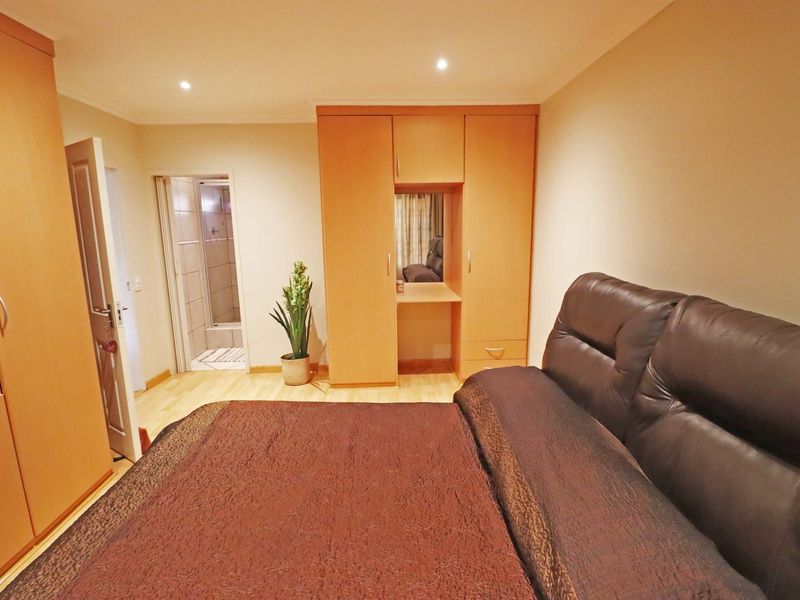 A bedroom featuring laminate flooring, built-in wooden cupboards with a vanity section, and direct access to an en-suite bathroom.