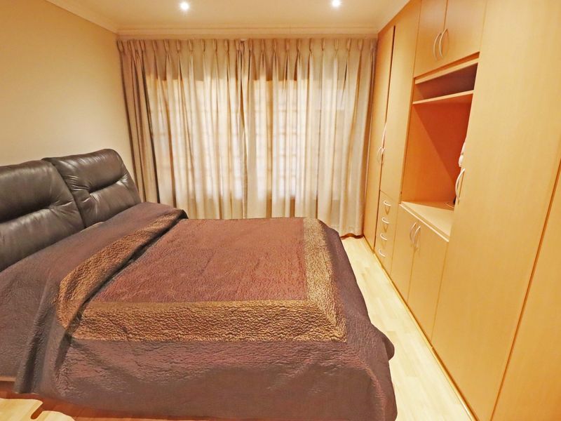 A bedroom featuring light-toned laminate flooring, recessed downlighting, and extensive built-in wooden cabinetry for storage.