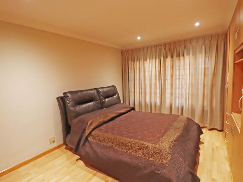 A well-maintained bedroom featuring light laminate flooring, built-in wooden cupboards, and recessed ceiling lighting with full-length window curtains.