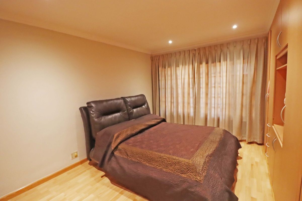 A well-maintained bedroom featuring light laminate flooring, built-in wooden cupboards, and recessed ceiling lighting with full-length window curtains.