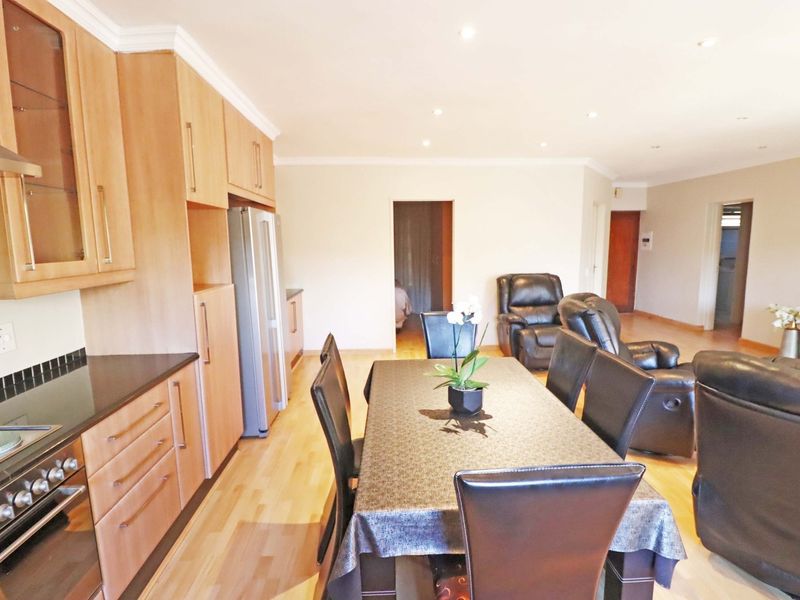 Open-plan living and dining area featuring light wood laminate flooring, recessed lighting, and a functional kitchen with built-in cabinetry and appliances.