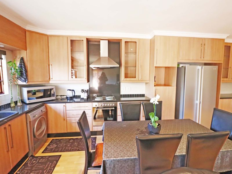 Open-plan kitchen and dining area featuring light wood cabinetry, granite countertops, integrated appliances, and laminate flooring.