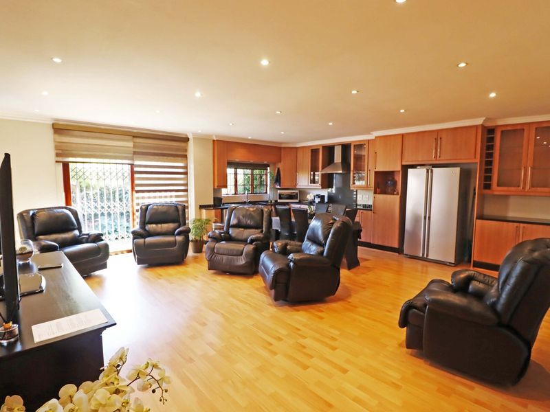 Spacious open-plan living area featuring warm wooden flooring, recessed lighting, and a well-appointed kitchen with ample wooden cabinetry and integrated appliances.