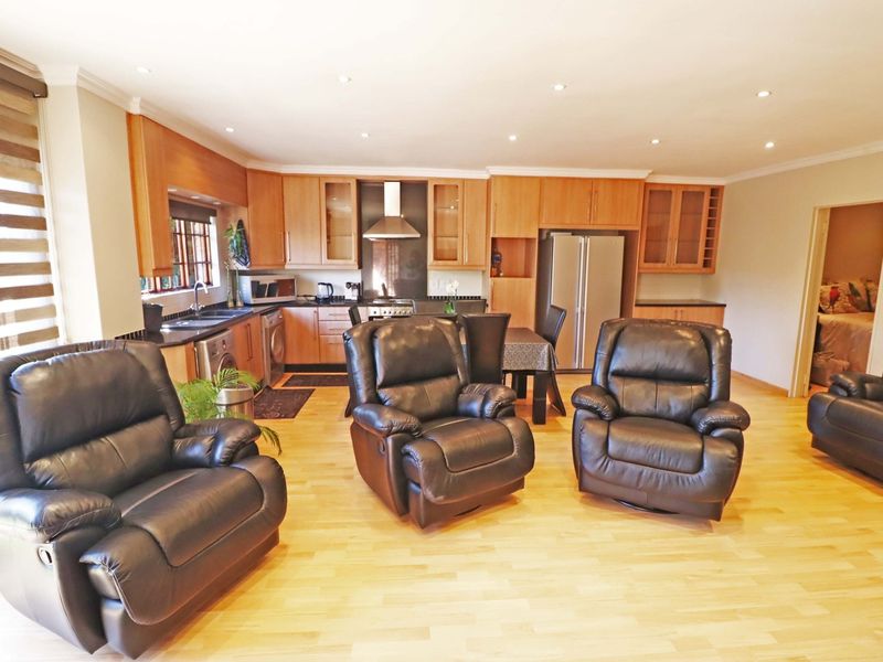 Spacious open-plan living area featuring a functional kitchen with wooden cabinetry, integrated appliances, and light laminate flooring throughout.