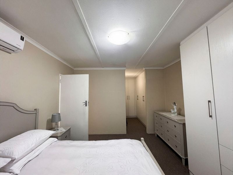 A well-maintained bedroom featuring built-in cupboards, neutral wall finishes, carpeted flooring, and a wall-mounted air conditioning unit.