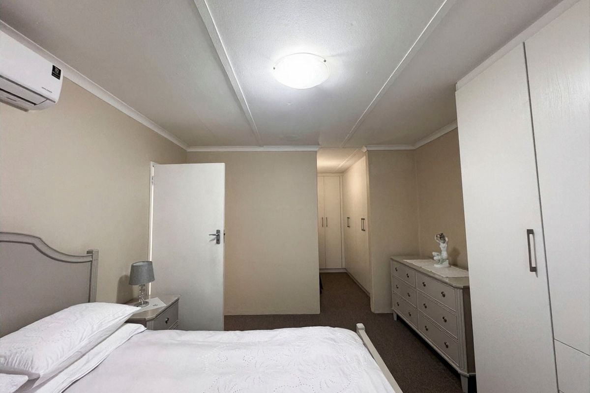 A well-maintained bedroom featuring built-in cupboards, neutral wall finishes, carpeted flooring, and a wall-mounted air conditioning unit.