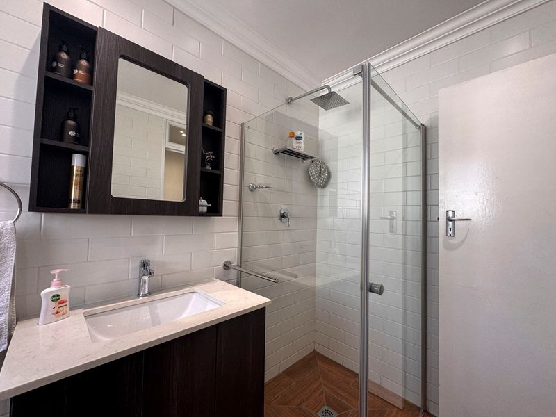 Modern bathroom featuring a vanity with stone countertop, wall-mounted storage, and a glass-enclosed shower with subway tile finishes.