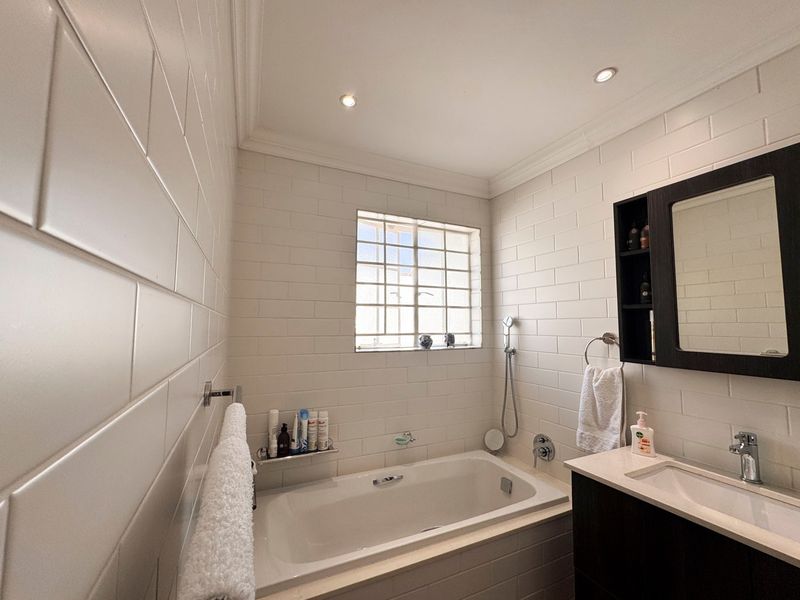 A well-maintained bathroom featuring a built-in bathtub, modern vanity with integrated sink, wall-mounted mirror cabinet, and classic white subway-style wall tiling.